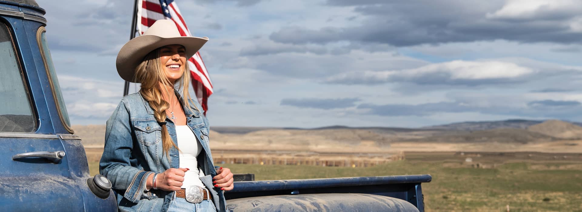 girl in front of American flag wearing belt buckle and cowboy hat