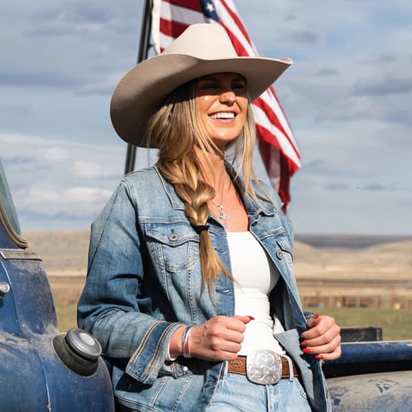 girl in front of American flag wearing belt buckle and cowboy hat